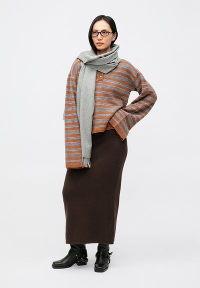 Ριγέ καφέ και γκρι υπερμεγέθη πουλόβερ, γκρι κασκόλ, καφέ μίντι φούστα, μαύρα μποτάκια αστραγάλου με λεπτομέρειες αλυσίδας. Ομαλές υφές, άνετη εφαρμογή.