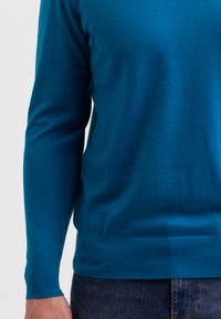 Teal tröja med lång ärm, mjukt stickat material, ribbade mudd och midja, stylad med mörka jeans.