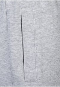 Grauer Sweatshirtstoff mit glatter Textur. Verfügt über eine rechteckige Seitentasche mit einer dezenten Naht. Das Material wirkt weich und angenehm zu tragen.