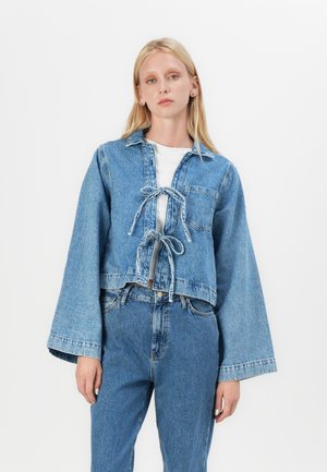 Light blue denim cropped jacket with wide sleeves, tie-front closure, and a chest pocket; paired with matching high-waisted jeans.