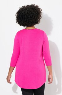 Langärmliges, rundhalsiges Oberteil in leuchtendem Pink, aus einem glatten, leichten Stoff gefertigt. Mit einem gewellten Saum und einer lockeren Passform.