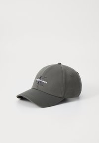 Grå caps laget av stoff med en buet skygge. Har brodert «Calvin Klein Jeans» tekst i hvitt og en logo i mørkeblå.