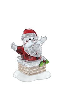 Figurita de Papá Noel con traje rojo y gorro, con barba y bigote blancos, brazos levantados, de pie en una chimenea decorada con hojas de acebo y bayas.