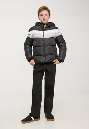 Czarna i szara pikowana kurtka z poziomymi paskami, zapinana na zamek błyskawiczny, z kapturem. Połączona z czarnymi spodniami i czarnymi butami z białymi akcentami.