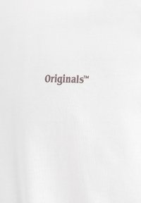 Witte katoenen t-shirt met "Originals™" in donkerbruine letters, centraal aan de voorkant gedrukt. Soepele textuur, standaard pasvorm.