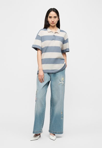 Polo rayé bleu clair et beige, coupe décontractée. Jean à jambes larges bleu clair avec broderies florales et détails usés. Talons blancs.