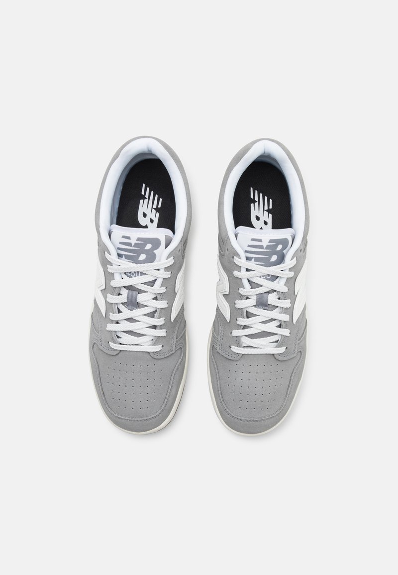 Baskets de sport grises avec des lacets et des accents blancs, présentant une boîte à orteils perforée et un intérieur noir rembourré avec un logo.