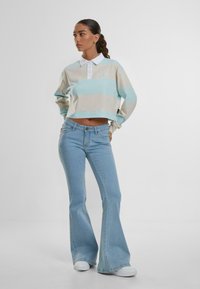 Polo à manches longues, coupé, en rayures bleu clair et beige avec un col blanc et un logo ; associé à un jean légèrement évasé bleu clair et des chaussures blanches.