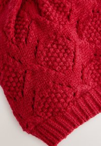 Tissu tricoté rouge avec un motif texturé de carrés en relief et des bords côtelés. Matériau doux et épais visible partout.