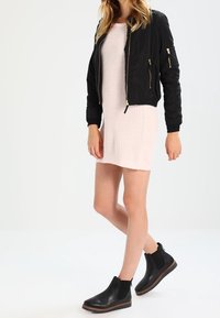 Giubbotto bomber nero con tasche con zip, abbinato a un vestito lavorato a maglia rosa chiaro e stivali Chelsea neri con suola testurizzata.