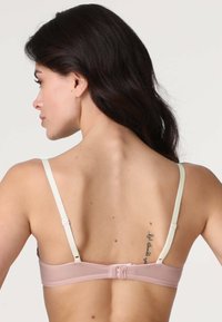 Reggiseno in tessuto rosa con spalline bianche regolabili, dotato di chiusura a gancio sul retro e texture liscia. Tatuaggio evidente.