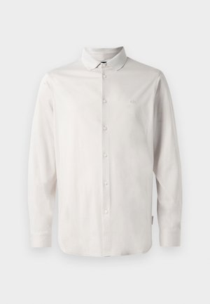 Camisa blanca de botón de manga larga con cuello y sutil logo "A|X" bordado en el lado izquierdo del pecho.