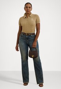 Polo en tricot beige, jeans taille haute bleus, ceinture marron et sac à main foncé. Sur fond clair. Sandales à bout ouvert.