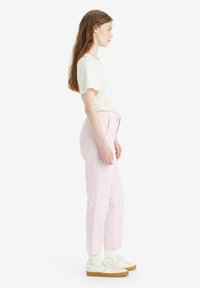 Pantaloni dritti rosa chiaro con dettagli delle cuciture anteriori, abbinati a una t-shirt crema e sneakers bianche con suola color nocciola.