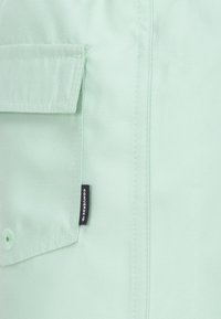 Lichtgroene shirt met een groot borstzakje, zichtbare stiksel details en een klein zwart label met de tekst "Converse".