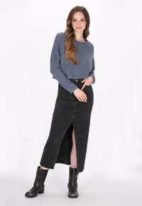 Pull en tricot bleu court, jupe en denim noir avec fente à l'avant, bottines noires avec des lanières, disposées sur un fond blanc.