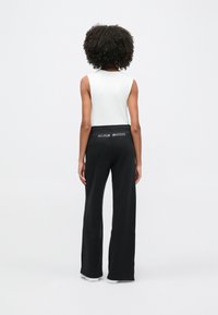 Světle šedé tílko spojené s černými tepláky se stahovací šňůrkou a nápisem "NIKE SHOX" na pasu. Plochá, hladká textura.