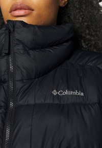 Zwarte pufferjas met hoge kraag, ritssluiting en Columbia-branding in zilverdraad op de borst, met een gladde textuur.