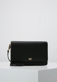 Sort pebblelæder crossover taske med et guldfarvet logo, fold-over design, aftagelig rem og en glat tekstureret overflade.