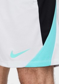Witte sportieve shorts met zwart en lichtblauwe accenten. Kenmerkend is de textuur van de stof en het lichtblauwe Nike-logo aan de onderzijde links.