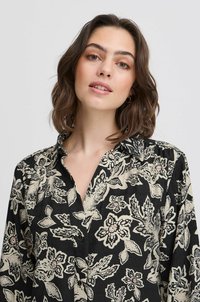 Blusa nera con motivi floreali nelle tonalità crema, con chiusura frontale a bottoni e colletto classico. Realizzata in tessuto leggero.