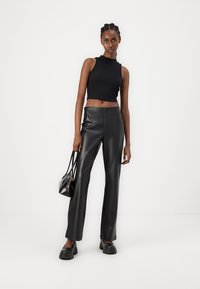Black sleeveless crop top with a high neck, paired with high-waisted black faux leather pants and chunky black shoes. Small black handbag.