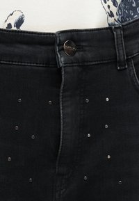 Pantalon en jean noir avec de petits clous argentés éparpillés sur le devant et une fermeture par bouton en métal portant la mention "MARCIAN."