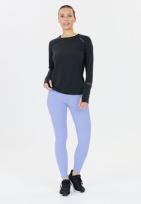 Lättvikts svart långärmad topp med reflexdetaljer, tillsammans med lavendelfärgade leggings med prickigt mönster och svarta träningsskor.