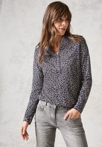 Chemise à manches longues en bleu marine foncé avec un motif de feuilles abstrait blanc, dotée d'un col et d'une coupe décontractée, associée à un jean en denim gris.