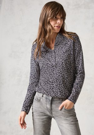 Chemise à manches longues en bleu marine foncé avec un motif de feuilles abstrait blanc, dotée d'un col et d'une coupe décontractée, associée à un jean en denim gris.