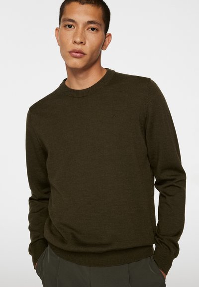 Olivgrön stickad tröja med rund halsringning, ribbad mudd och nederkant, med en liten, diskret logotyp på bröstet. Lätt textur.