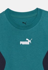 Τυρκουάζ μπλούζα Puma με λαιμόκοψη crew, με λευκό κεντητό λογότυπο Puma και μαύρο τυπωμένο λογότυπο Puma στο εσωτερικό της λαιμόκοψης.