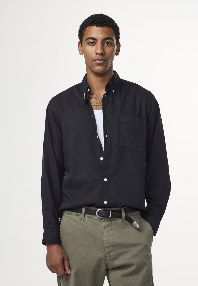 Chemise noire à boutons avec une poche poitrine, un col et des manches longues. Associée à un pantalon vert olive et une ceinture noire.
