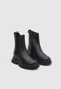 Botas de tobillo de cuero negro con textura suave, paneles laterales elásticos y suela de plataforma gruesa. Detalle de cremallera lateral para facilitar el uso.