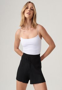 Vit, tight passande linne med tunna axelband som matchas med högmidjade, svarta ribbade shorts med dragsko i midjan och vågformad nederkant.