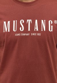 Bordová tričko z bavlny s kulatým výstřihem a výrazným bílým textem "MUSTANG JEANS COMPANY OD ROKU 1932."