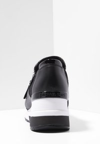 Sneaker in pelle nera e rete con una suola bianca, dotata di chiusura con zip e logo "Michael Kors" in rilievo sul tallone.