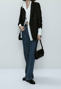 Blazer nero su una camicia bianca, abbinato a jeans blu a vita alta e a gamba larga e mocassini in pelle nera. Inclusa una borsa nera.