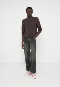 Ciemnoszare dżinsy z kontrastującym przeszyciem, zestawione z bordowym, prążkowanym swetrem. Modelka ma na sobie różowe tenisówki z płótna.