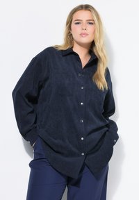 Camicia button-up in corduroy blu navy con maniche lunghe, due tasche sul petto e dettagli in metallo argentato. Presenta una vestibilità comoda e una texture morbida.