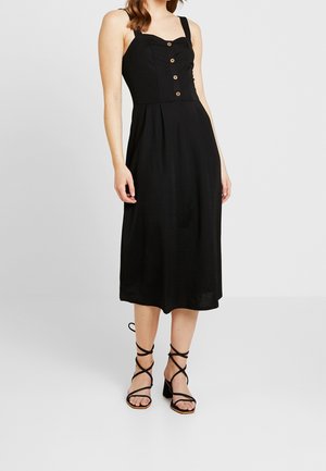 Czarna sukienka midi z dopasowanym gorsetem, kwadratowym dekoltem, pięcioma brązowymi guzikami i rozkloszowanym dołem. W zestawie z czarnymi sandałami na obcasie z paskami.