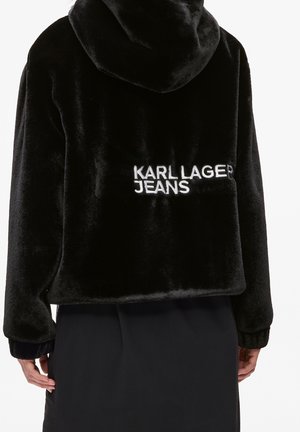 Czarna pluszowa bluza z kapturem z białym napisem "KARL LAGER JEANS" na plecach, noszona przez osobę widzianą od tyłu, na jednolitym tle.