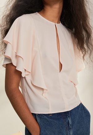 Blouse rose clair avec des manches courtes froncées, décolleté en V et détail de couture centrale, fabriquée dans un tissu lisse et léger.
