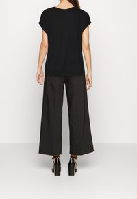 Top nero a maniche corte con scollatura rotonda abbinato a pantaloni neri dal taglio ampio. L'outfit è completato da scarpe con tacco nere lucide.