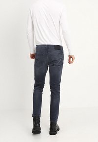 Tight fit, mörkblå denimjeans med fem fickor, subtila sömdetaljer och en svart midjeband. Parat med svarta ankelboots.