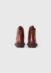 Bottes chelsea en cuir marron avec des panneaux élastiques ton sur ton, des tirettes et une semelle en caoutchouc marron robuste. Vue de l'arrière montrant le design élégant.