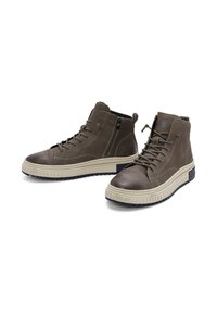 Hoge schoenen van donkerbruin leer met een gladde afwerking, voorzien van een contrasterende crème rubberen zool en een ritssluiting aan de zijkant.