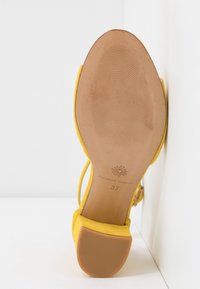 Semelle de sandale en daim jaune avec talon bas, embout de talon en caoutchouc texturé et logo Fabienne Chapot avec la taille 37 embossée sur la semelle.