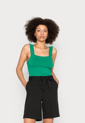 Top ajustado verde com alças franzidas, combinado com calções pretos de cintura alta com um laço na cintura. Linhas simples e limpas em cores sólidas.