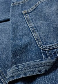 Gros plan sur un tissu en denim bleu montrant un revers plié et une poche cousue avec des détails en fil jaune.